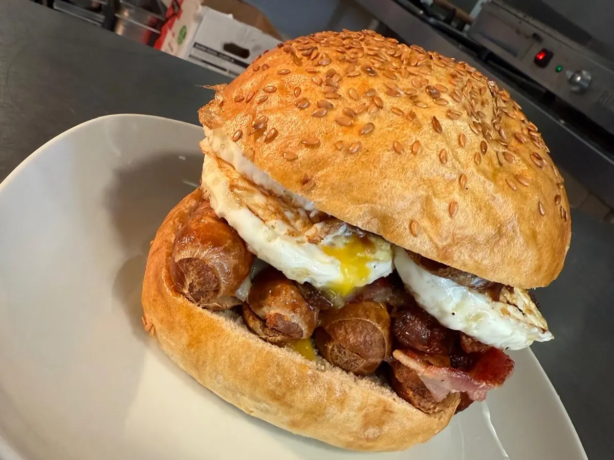 A seeded burger with bacon, cheese, and fried egg on a white plate.