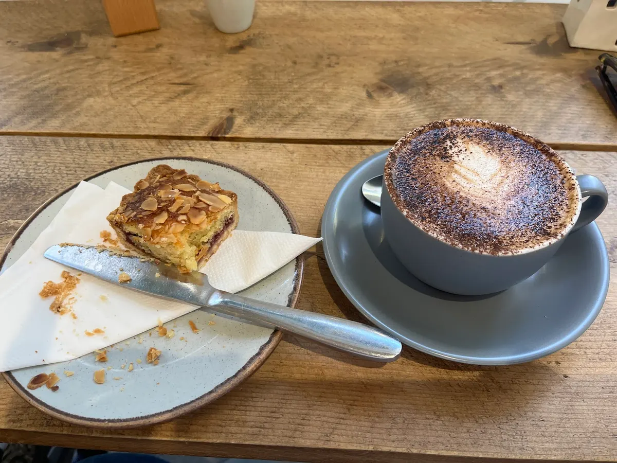 A slice of almond cake and a cappuccino with cocoa on a wooden table.