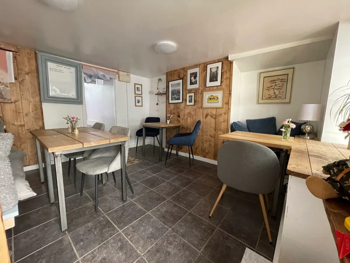 A warm, intimate dining room with wooden panelling, multiple tables, chairs, and framed artwork on walls.