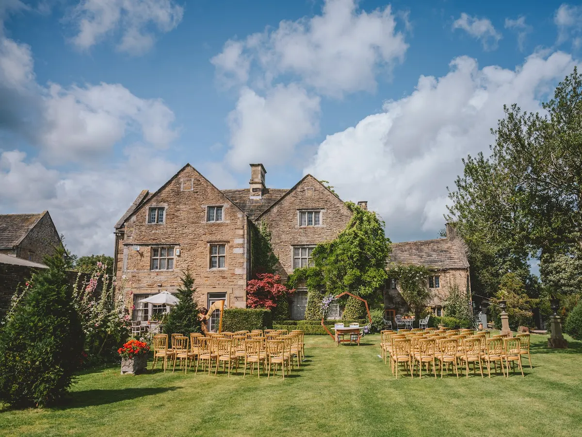 A stone country house with manicured grounds, wooden chairs arranged on the lawn for an event.