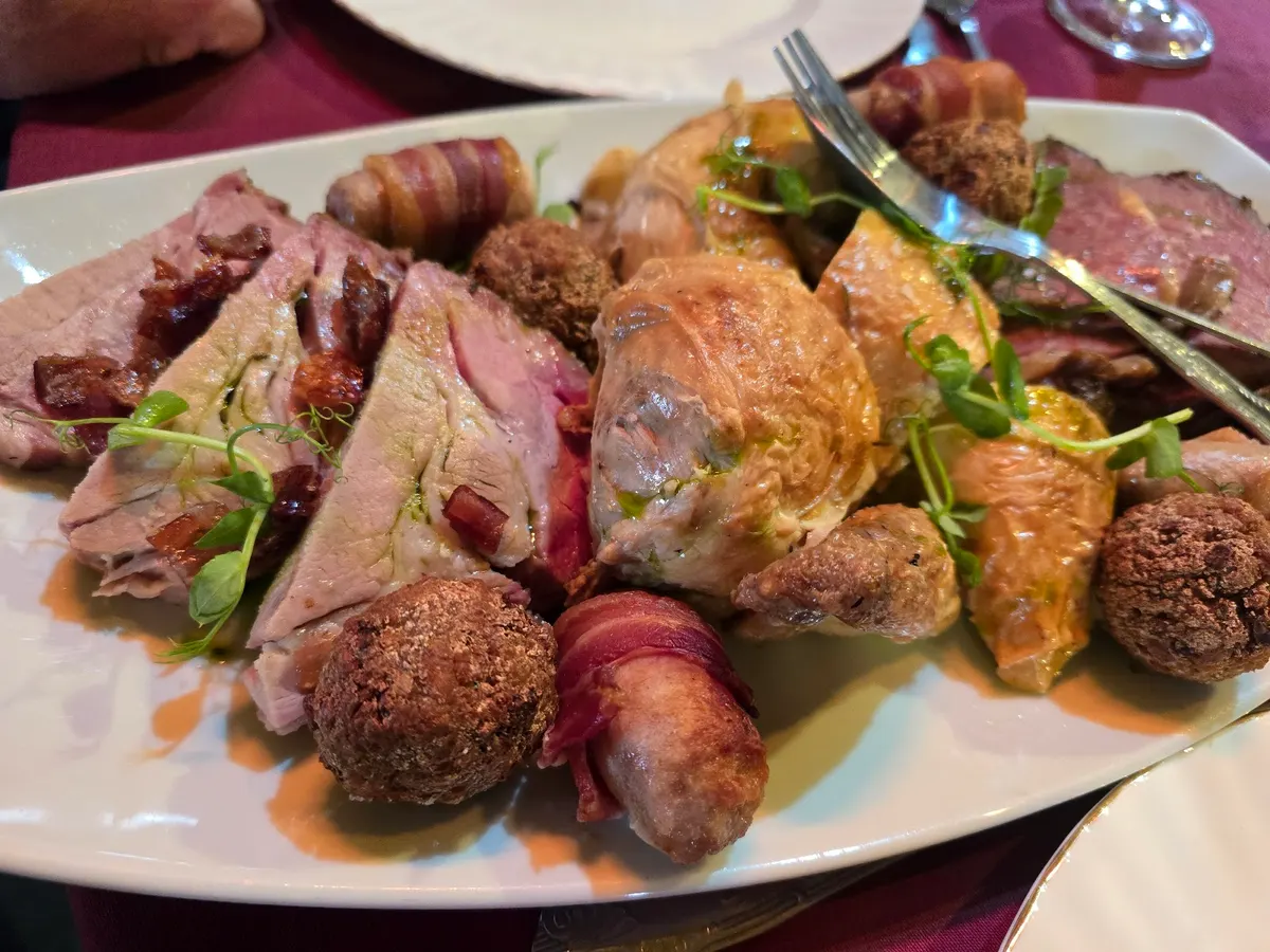 A fine dining plated course with sliced rare beef, potatoes, and vegetables with garnish.