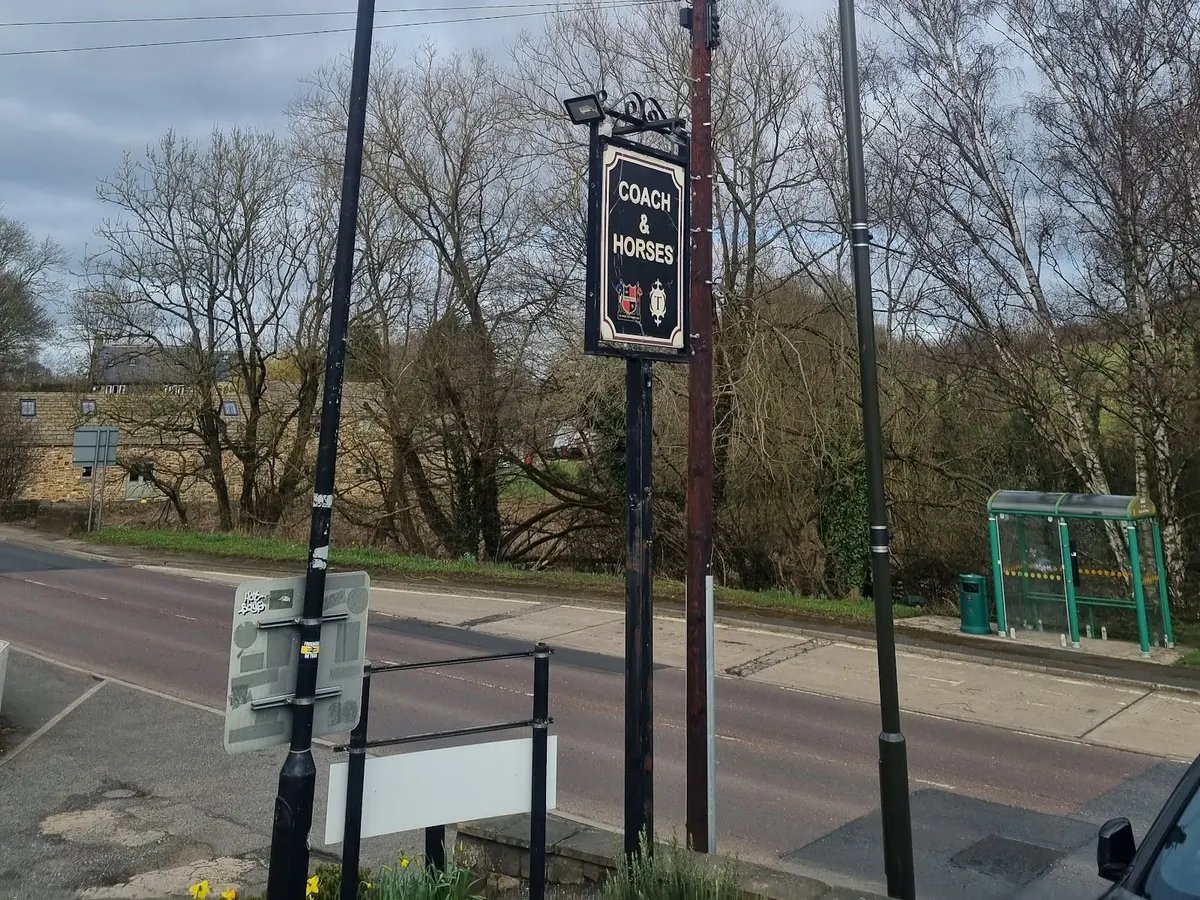 A hanging sign for Coach and Horses at the roadside, showing the business name and logo with bare trees in the background.