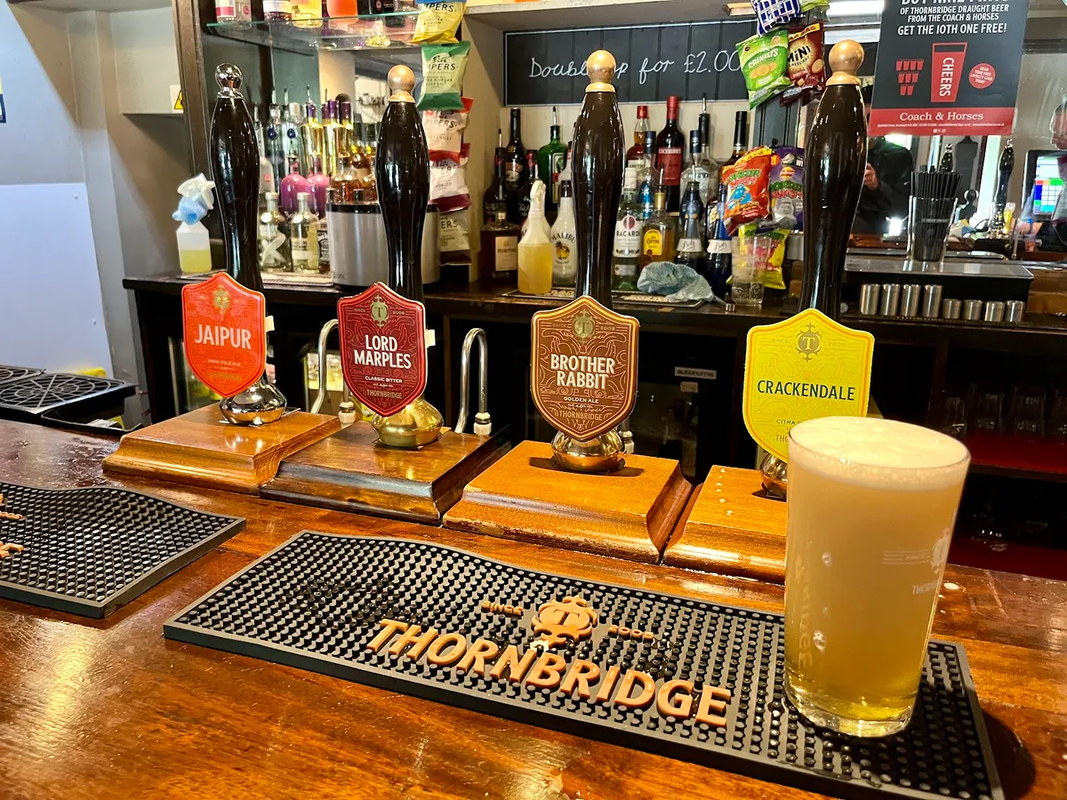 The bar of Coach and Horses Inn showing multiple beer pumps on display, with decorative signage and glasses on the shelf.
