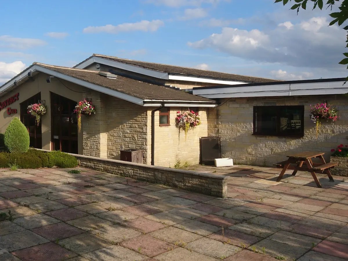 The exterior of Contact Club showing a modern stone building with a covered entrance and hanging flower baskets on a sunny day.