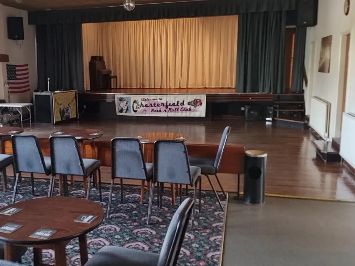 The interior of Contact Club showing a large hall with a stage, tables and chairs arranged for events, and decorative wooden panels.