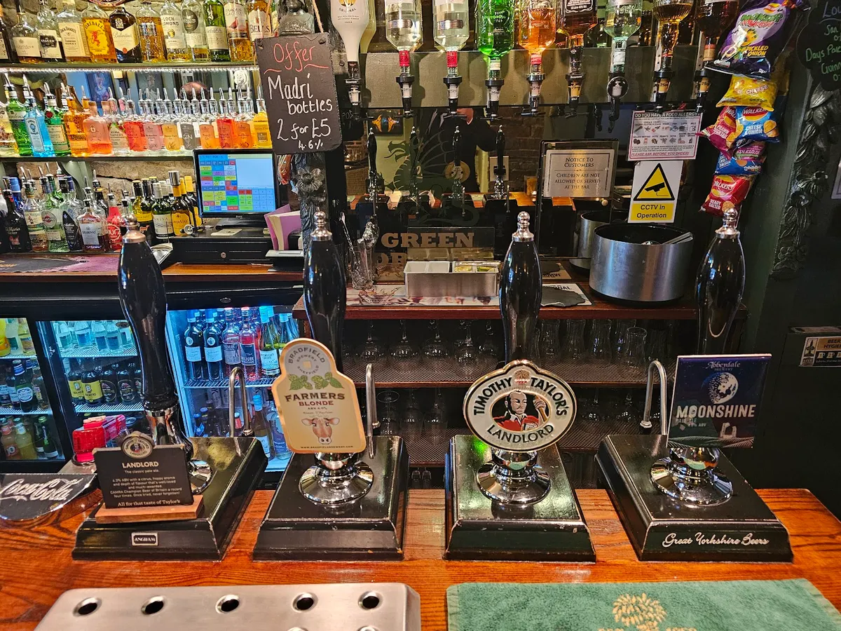 The bar counter of Green Dragon pub showing beer taps, bottles, and bar pumps with various beer brands.