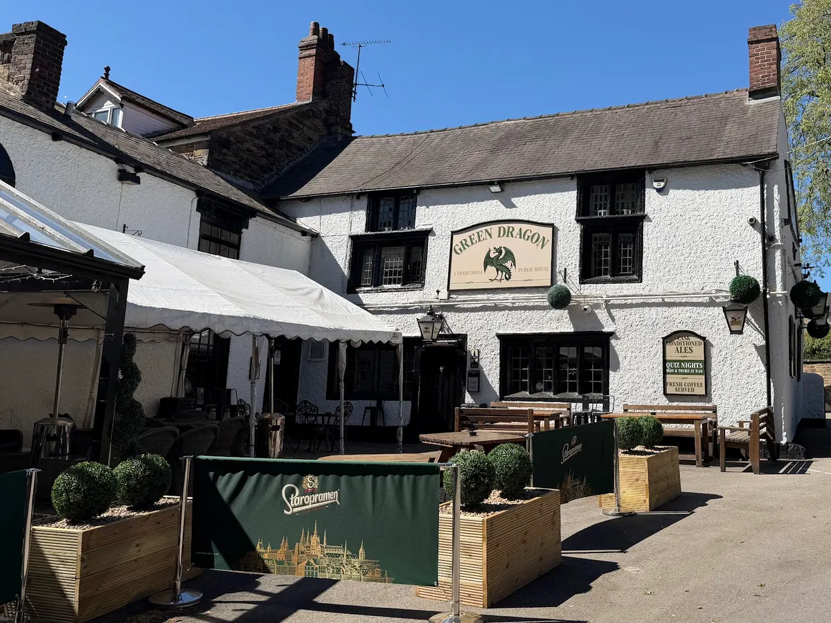 The front of the Green Dragon on Church Street, a white-painted stone building with a clear 'GREEN DRAGON' sign, showing outdoor seating with shade structures.