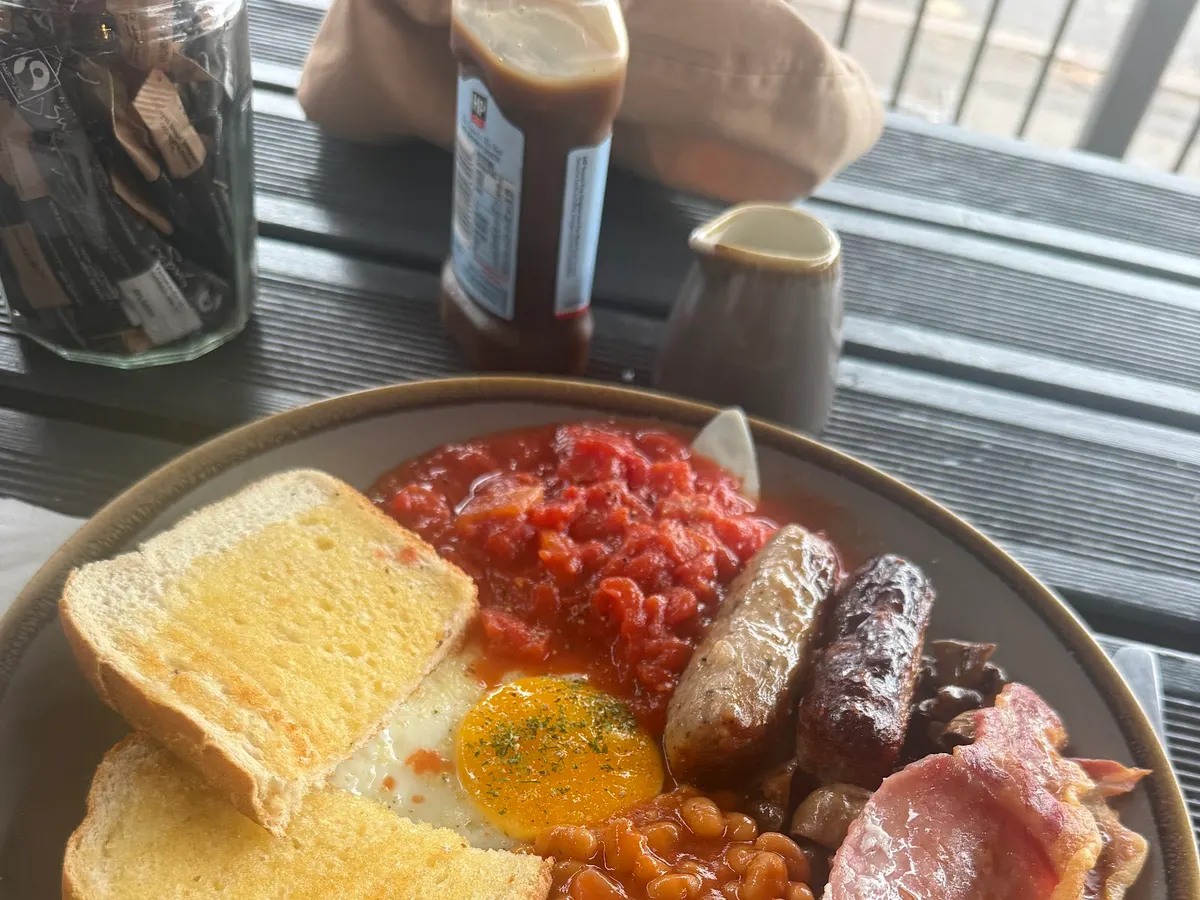 A full English breakfast on a plate with toast, fried egg, sausage, bacon, baked beans, and tomatoes.