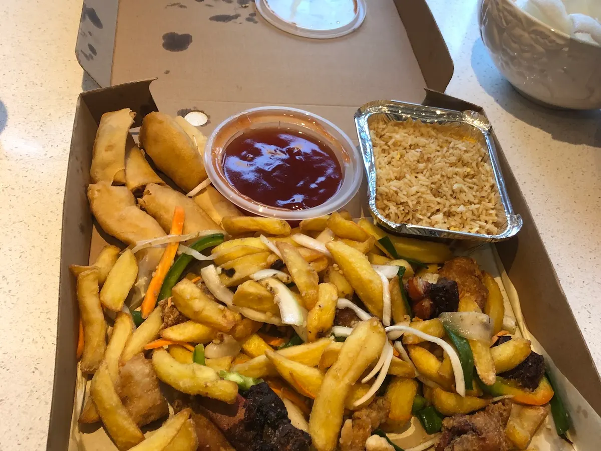 A Chinese takeaway meal in a cardboard box showing stir fried noodles and rice with vegetables and sauce.