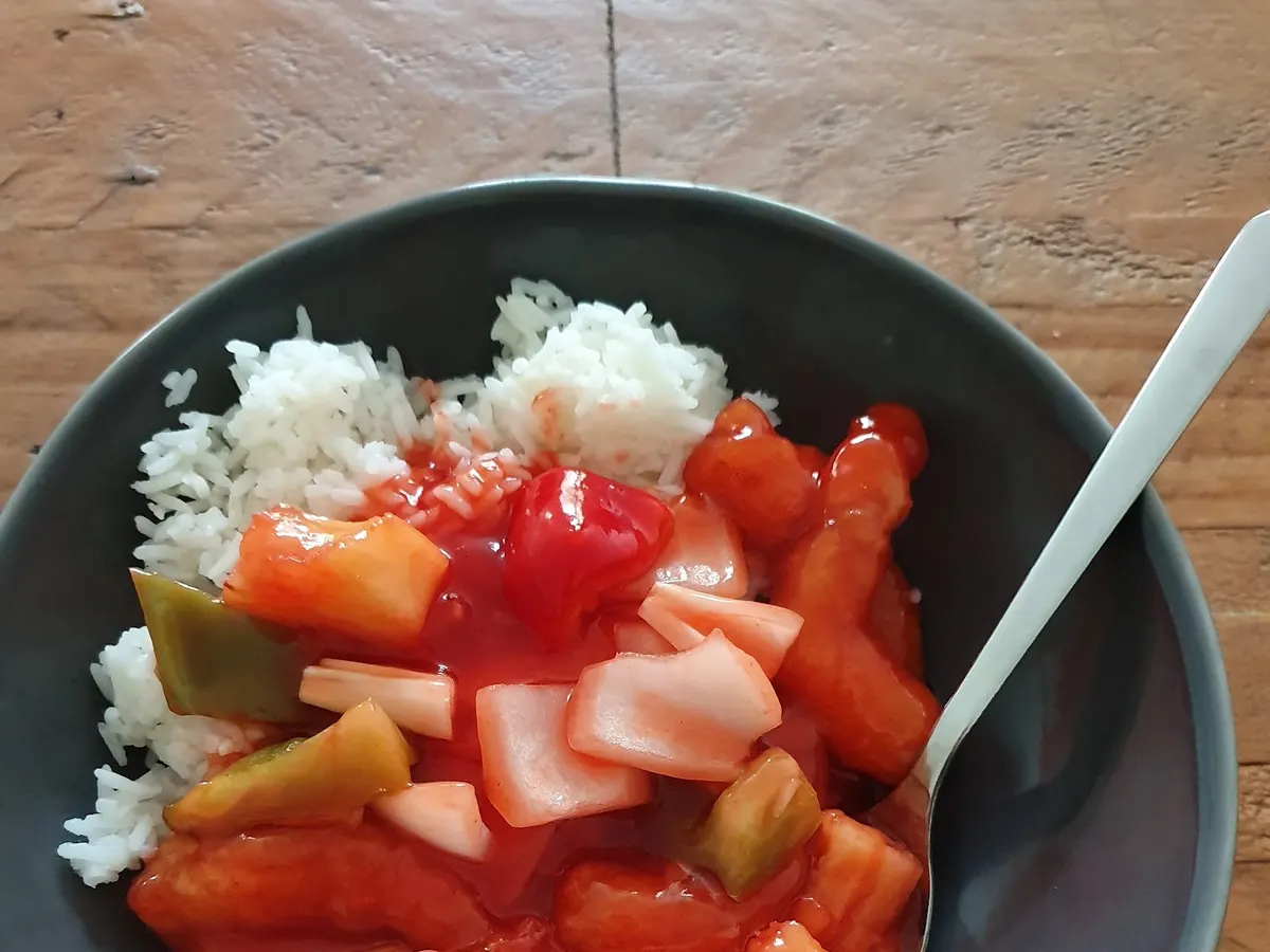 A bowl of white rice with stir-fried vegetables including red peppers, tomatoes, and cucumber.