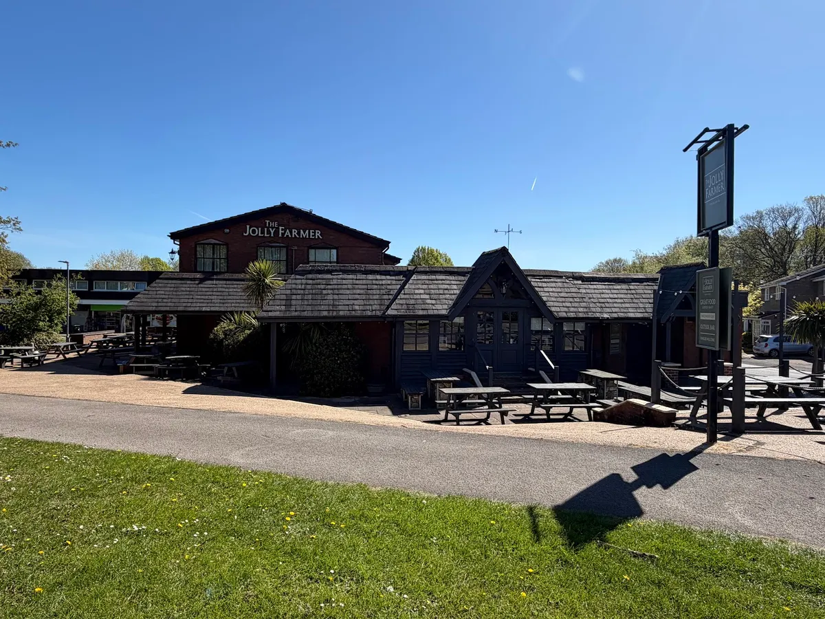 The Jolly Farmer pub building with clear signage, pale stone exterior, and landscaped grounds in bright daylight.