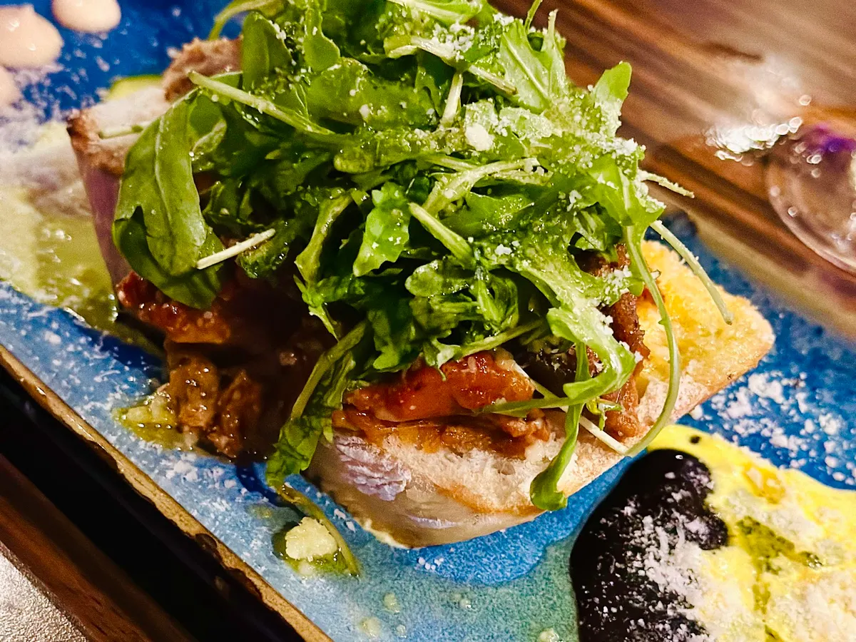 A carefully plated main course featuring seared fish with citrus garnish, charred vegetables, and artistic sauce on a blue-rimmed plate.