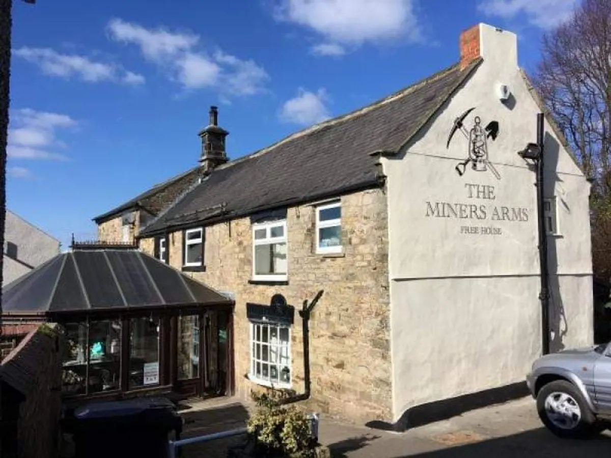 The Miners Arms pub building exterior with stone and cream rendered walls, slate roof, clear pub sign, and entrance with covered porch.
