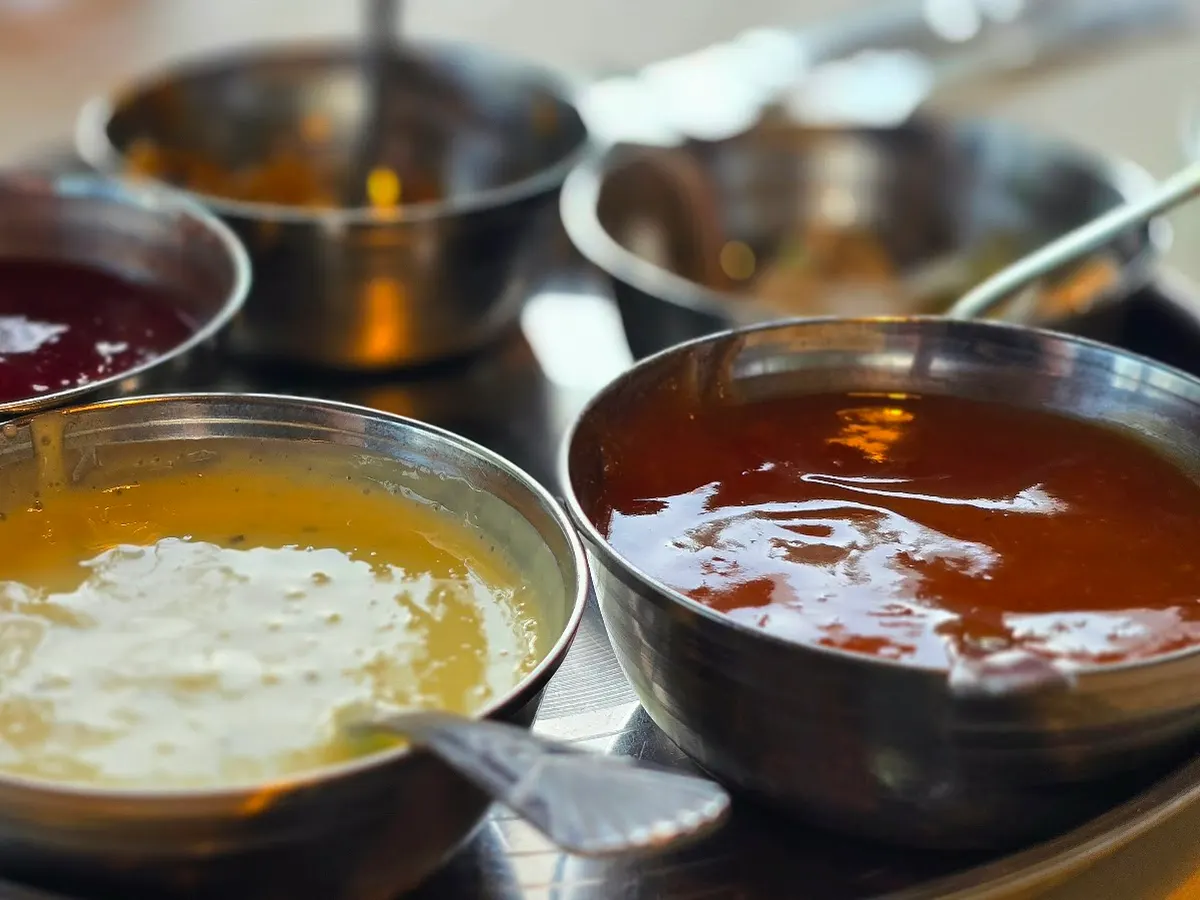 Multiple bowls of curried sauces and accompaniments displayed with contrasting colours ranging from deep brown to pale cream.