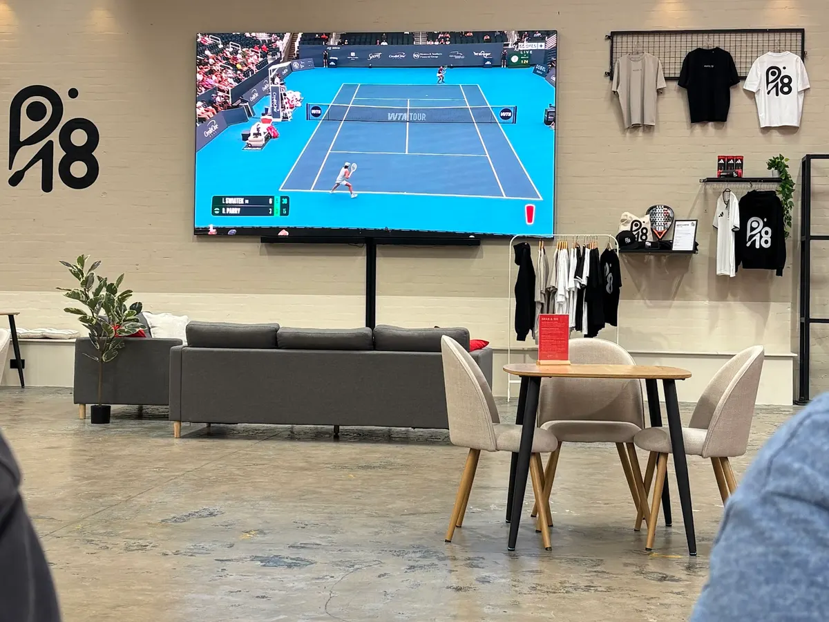 The P18 lounge with a grey sofa, a tennis match on a wall-mounted screen and P18 clothing on display.