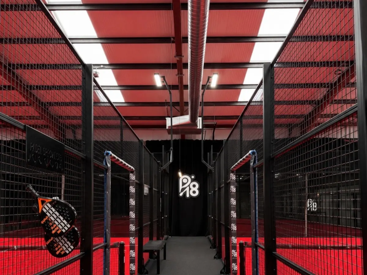 The indoor padel courts at P18, with red walls, black mesh fencing and the P18 logo at the far end.