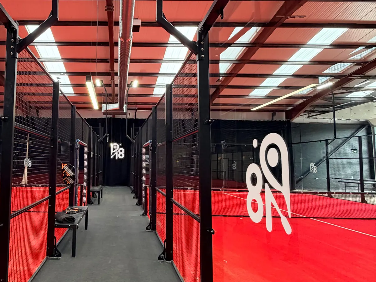 The indoor PADEL 18 courts with red surfaces and black mesh walls, with the P18 logo on the back wall.