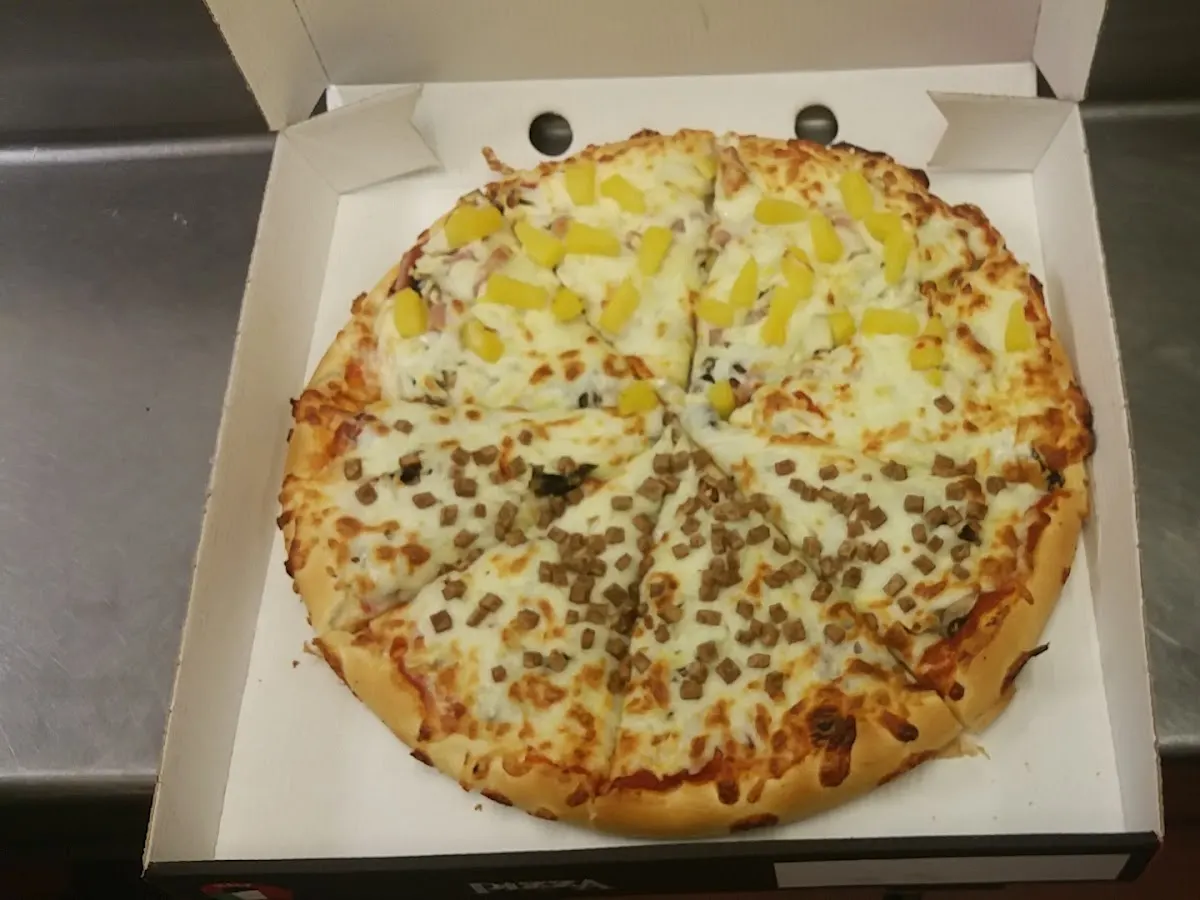 A pizza in a cardboard box showing melted cheese and toppings with yellow peppers visible.