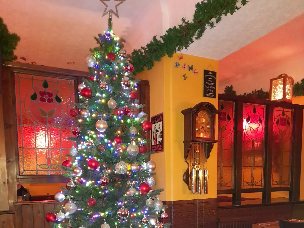 Inside the pub decorated for Christmas with a lit tree, colored ornaments, and red and orange themed interior decor.