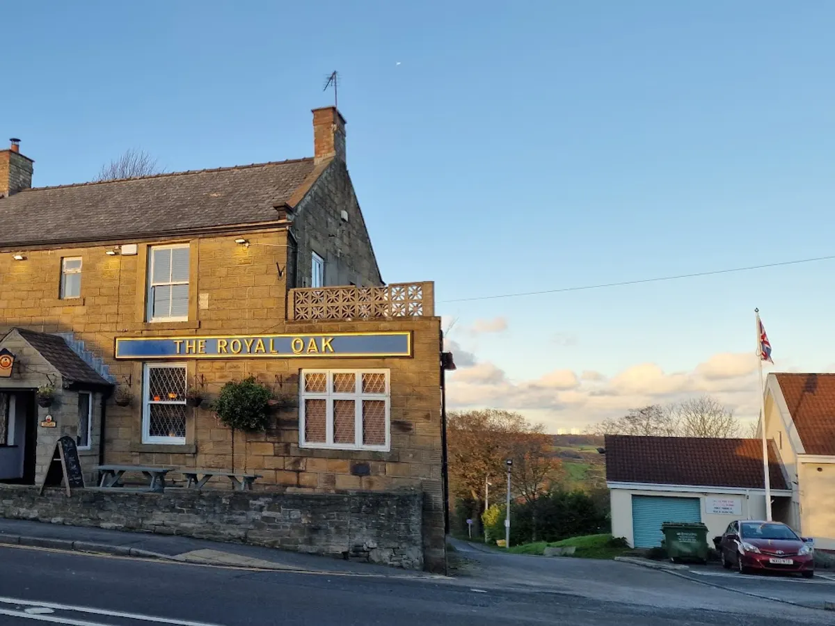 The Royal Oak Inn stone building during daytime showing the blue entrance doors, brass sign, and leaded windows.