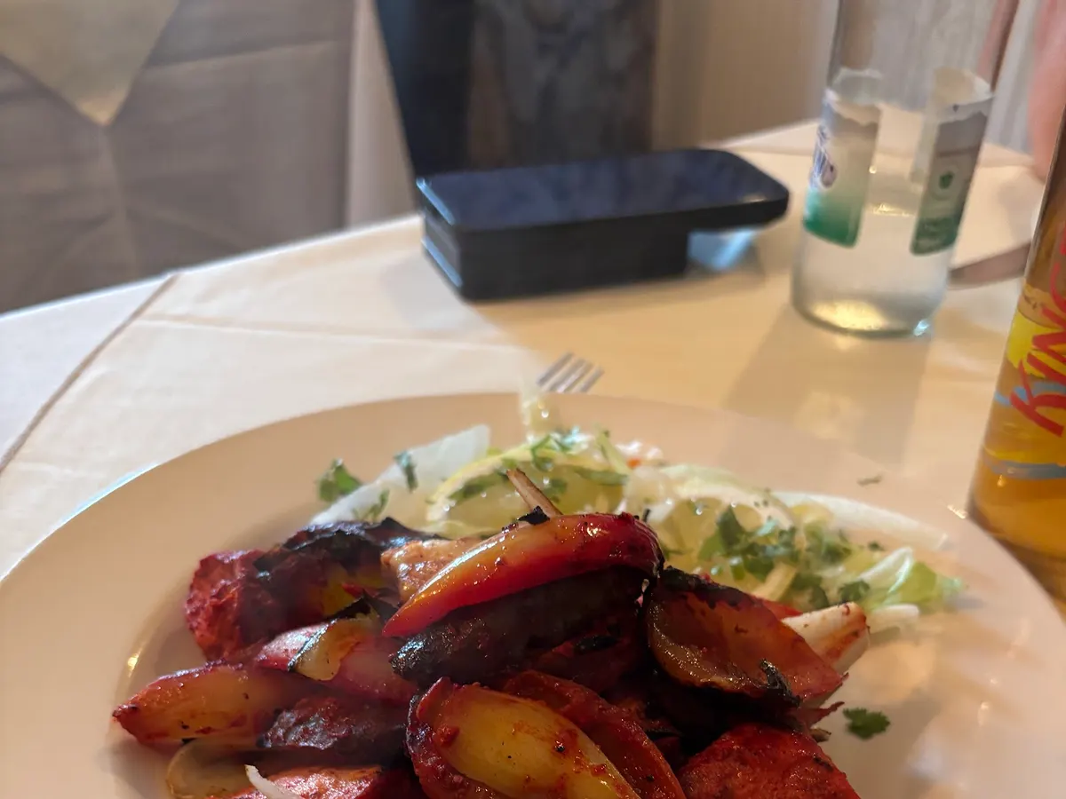 A plate of roasted duck with pepper slices and colored vegetables, with a glass of drink visible.
