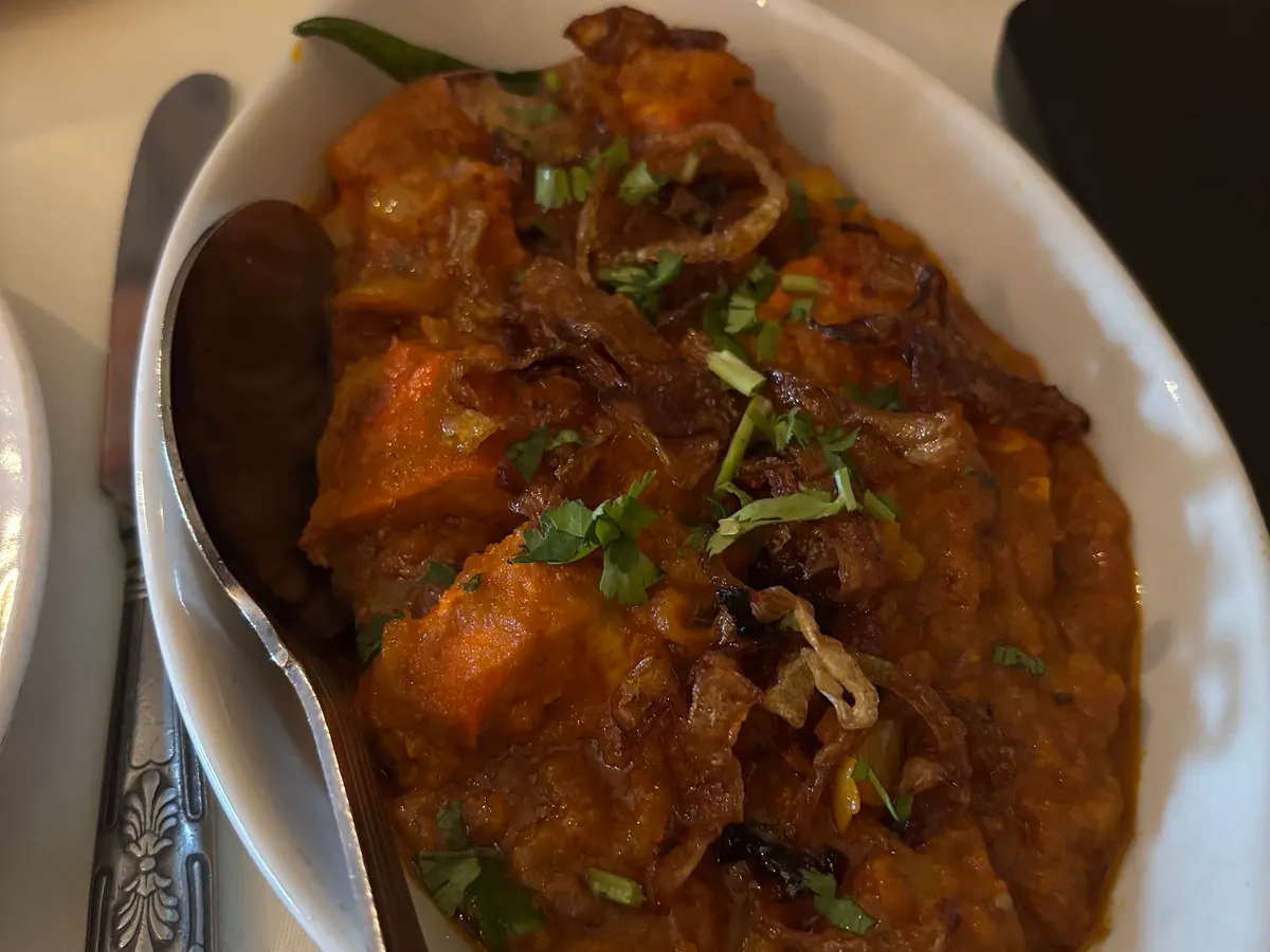 A bowl of Indian curry with chunks of meat and fresh cilantro garnish on top.