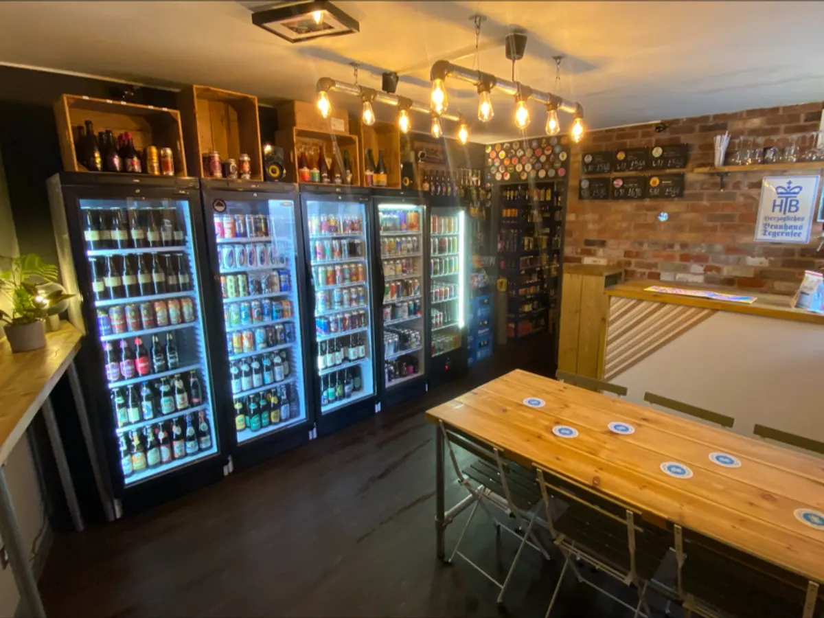 The inside of The Beer Stop with beer fridges, tables, and bar area lit by hanging lights.