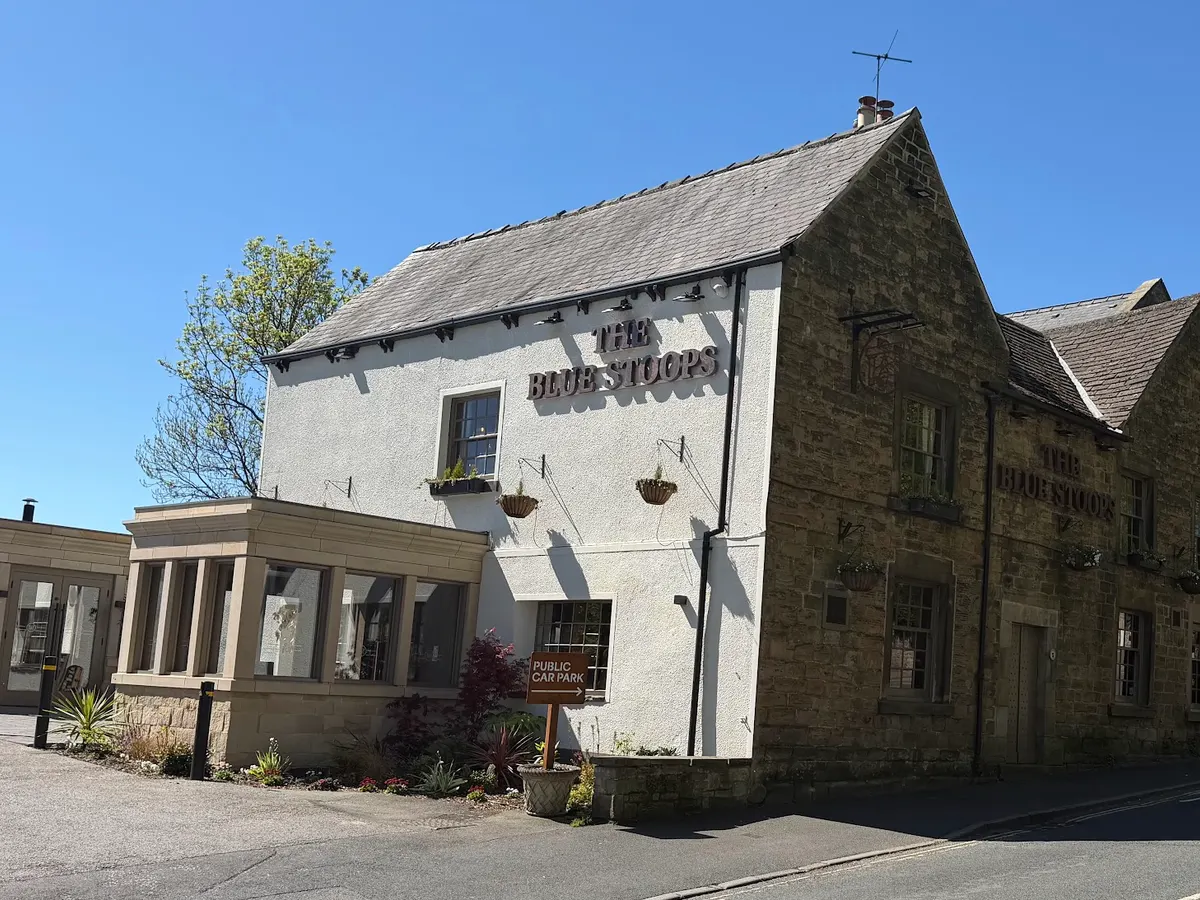 The front of The Blue Stoops pub showing the white and stone building with its hanging sign.
