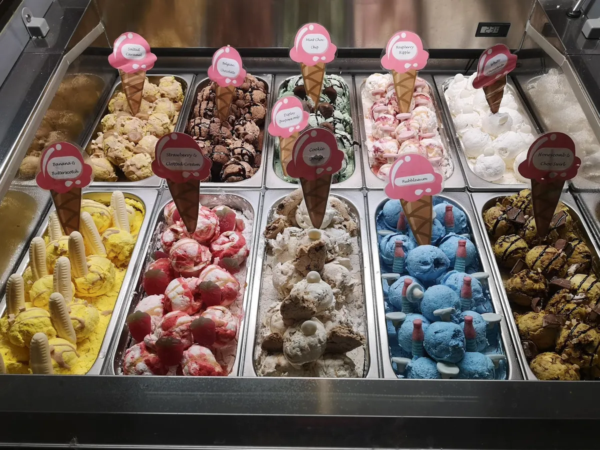An ice cream display case with many colorful flavours in metal bins.