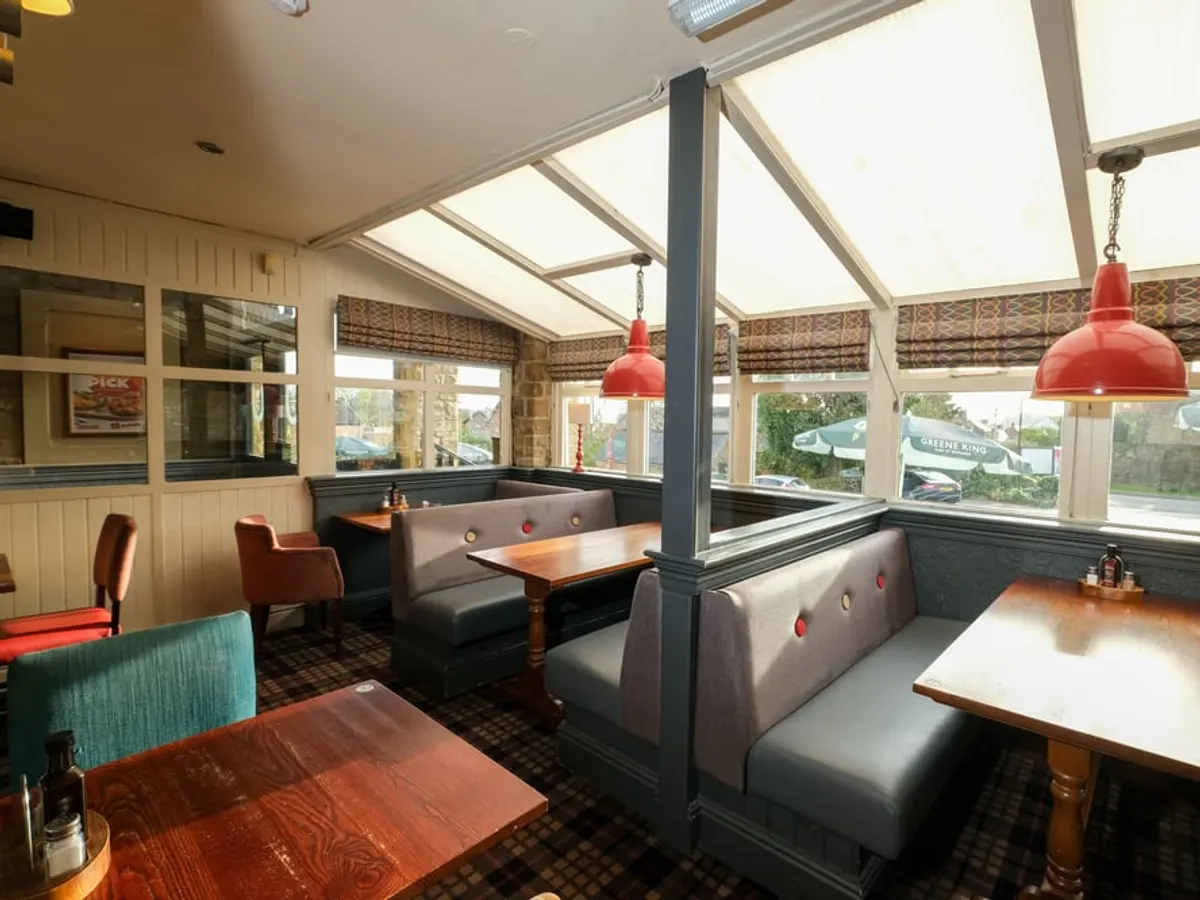 A bright conservatory dining space with red pendant lights, seating booths, and windows.