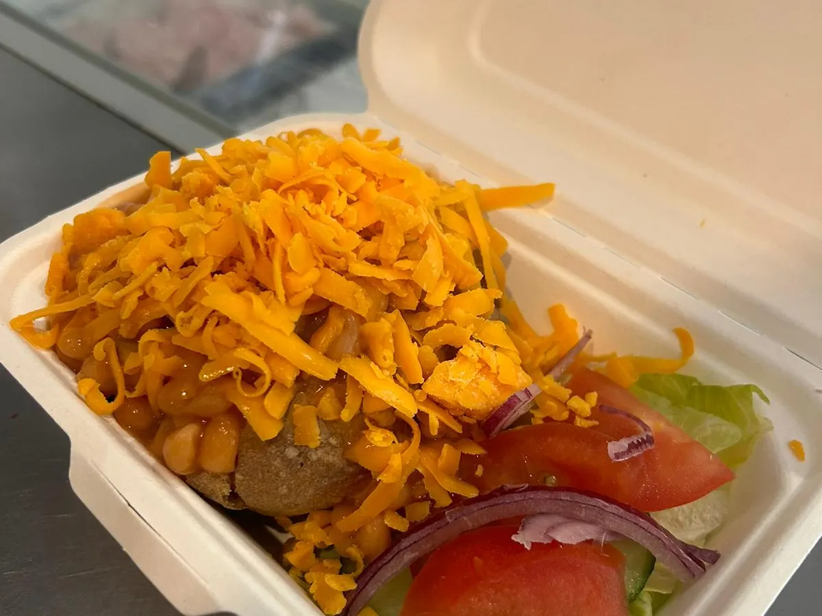 A loaded hotdog with crispy onions, lettuce, and tomato in a container.
