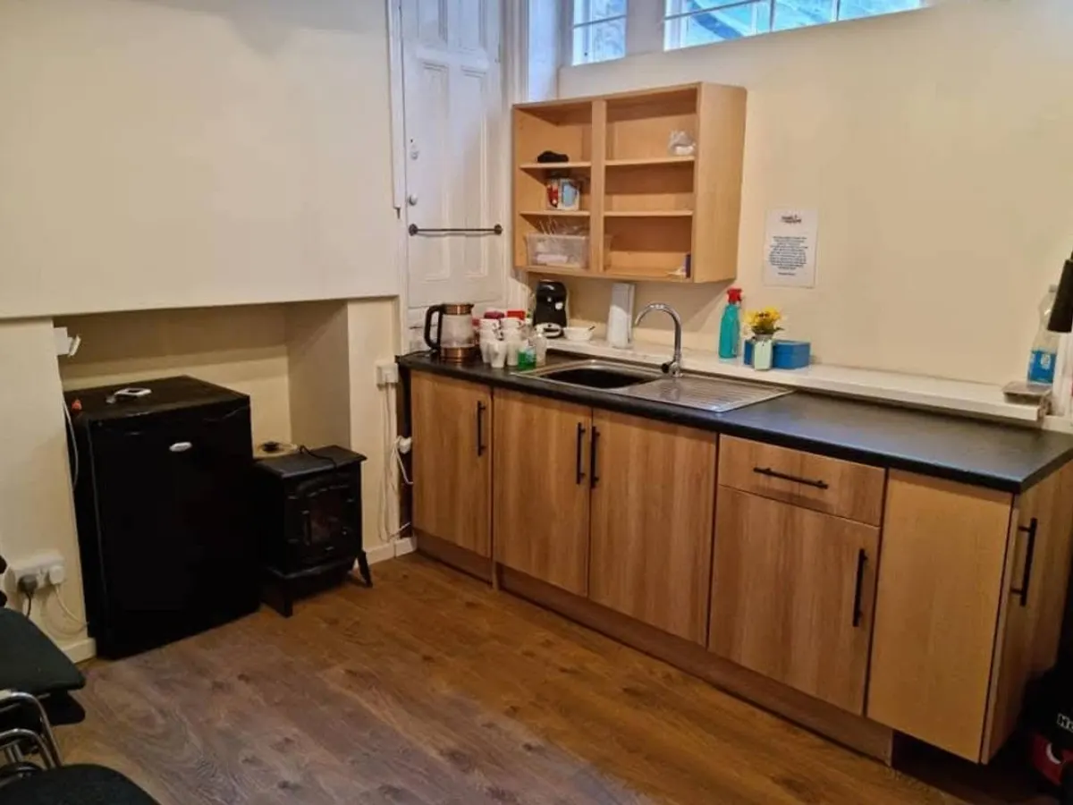 A kitchen area with wood-effect cupboards, a sink, a kettle and a black fridge.