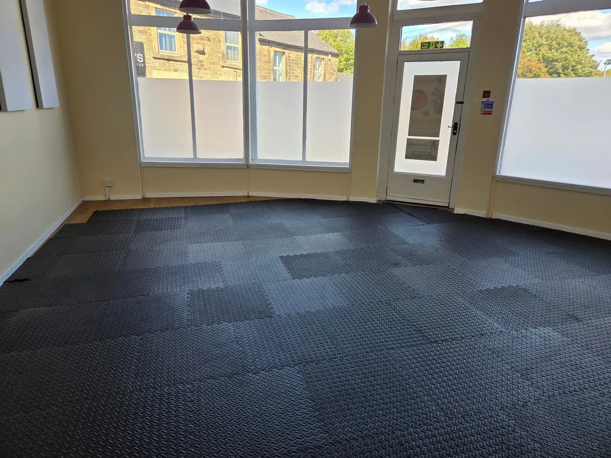 A large room with black interlocking floor mats, big windows and red pendant lights.
