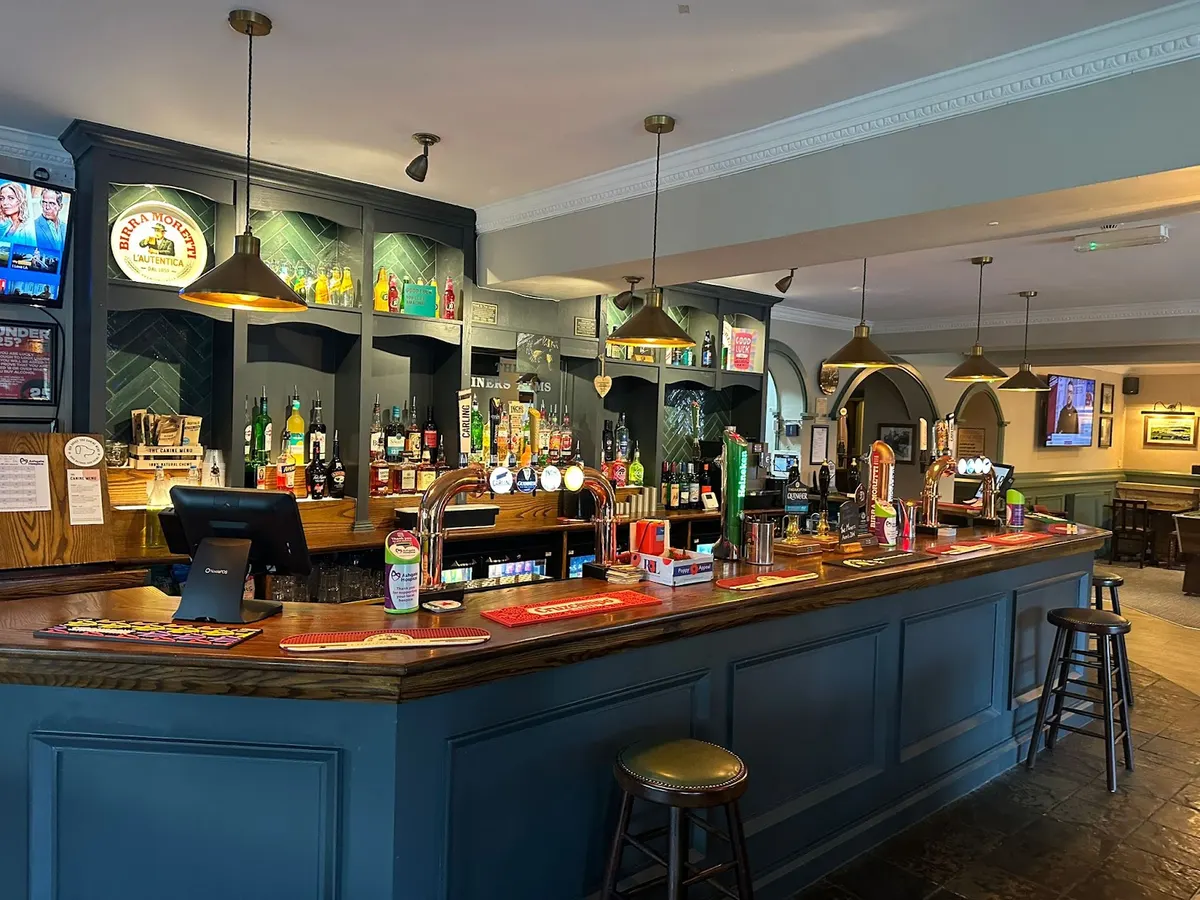 The bar area inside The Miners Arms with bottles displayed on shelves, brass beer taps, and pendant lights overhead.