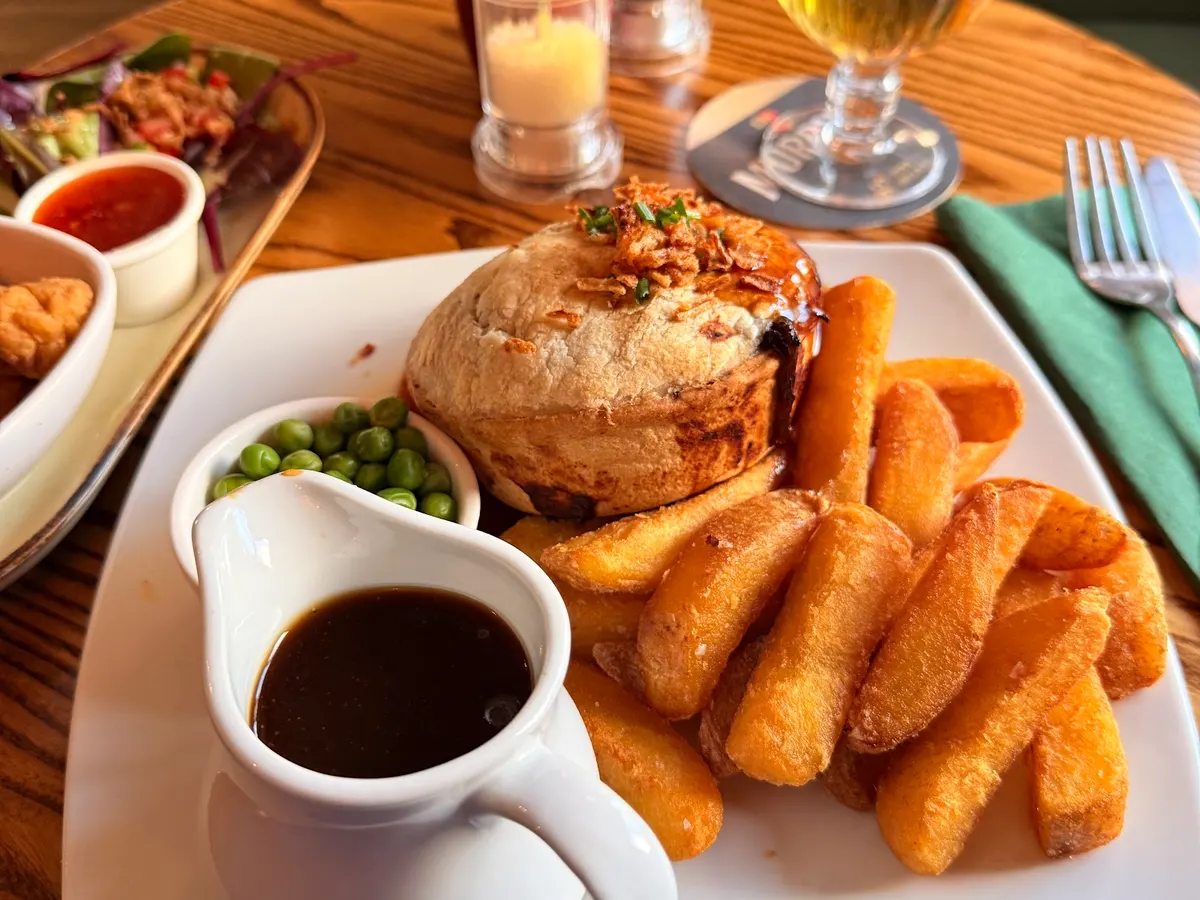 A plated meal at The Miners Arms showing a steak with gravy, peas, and chips served on a white plate.