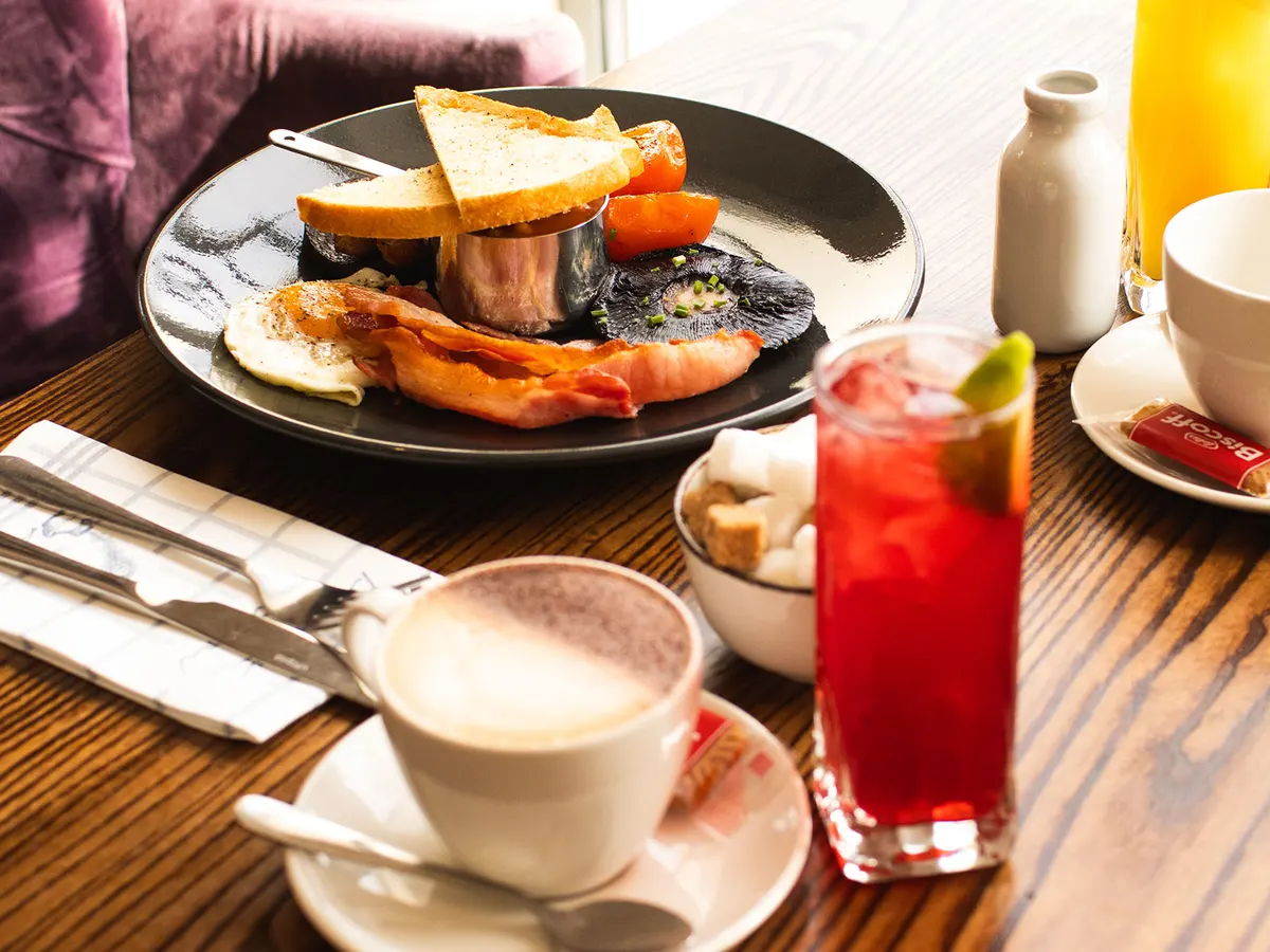 A cooked breakfast at the Peacock at Barlow, with a coffee and a glass of red juice on a wooden table.