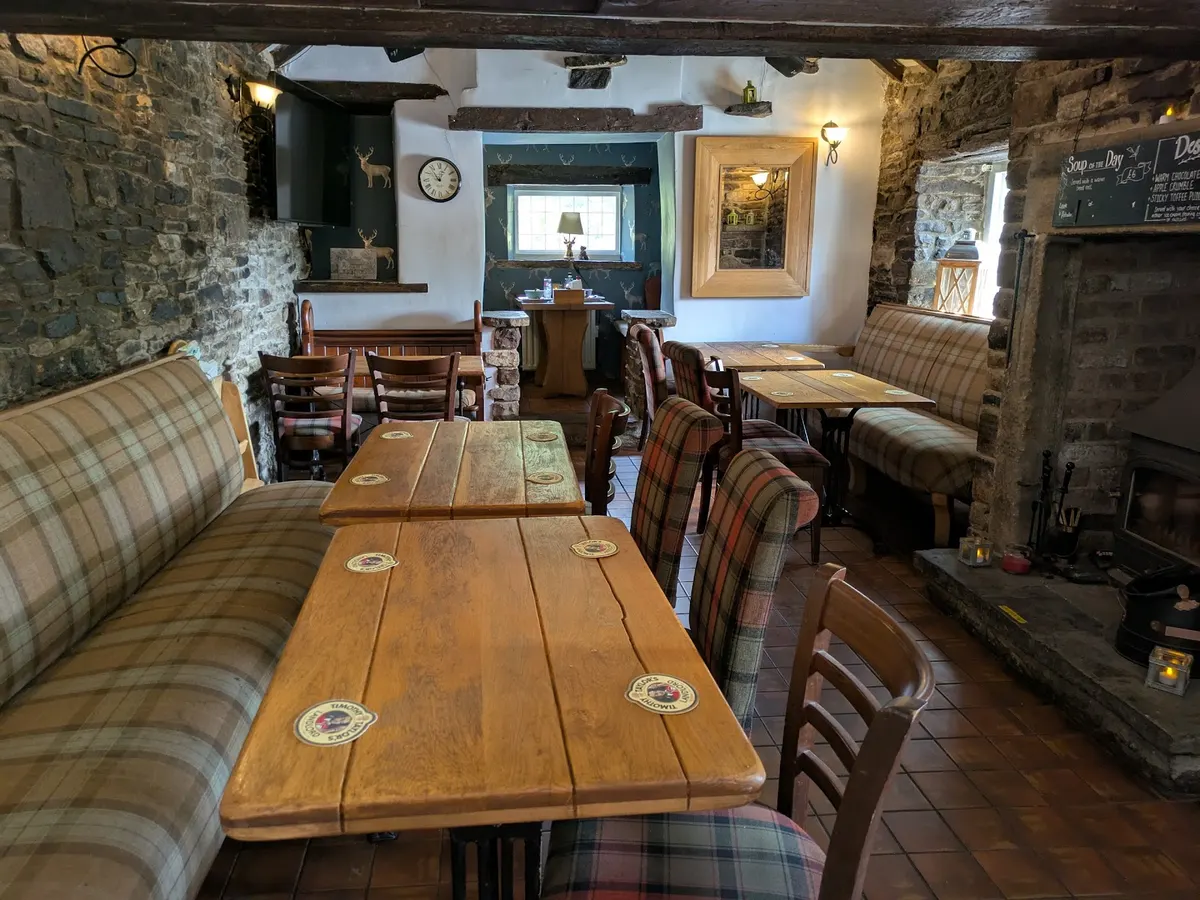 The interior of The Royal Oak showing tables with striped upholstered seating, wooden beams, stone walls, and a cozy traditional pub atmosphere.