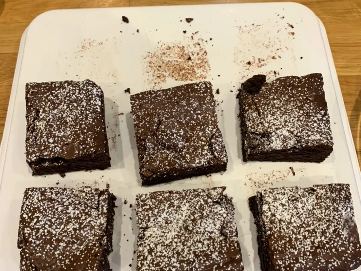 Six chocolate brownies dusted with icing sugar arranged on a white plate at The Snug café.