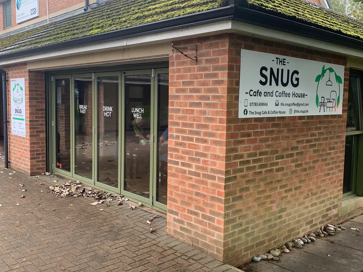 The front of The Snug Café and Coffee House showing the brick building, glass doors, and the sign with the cafe logo clearly visible.