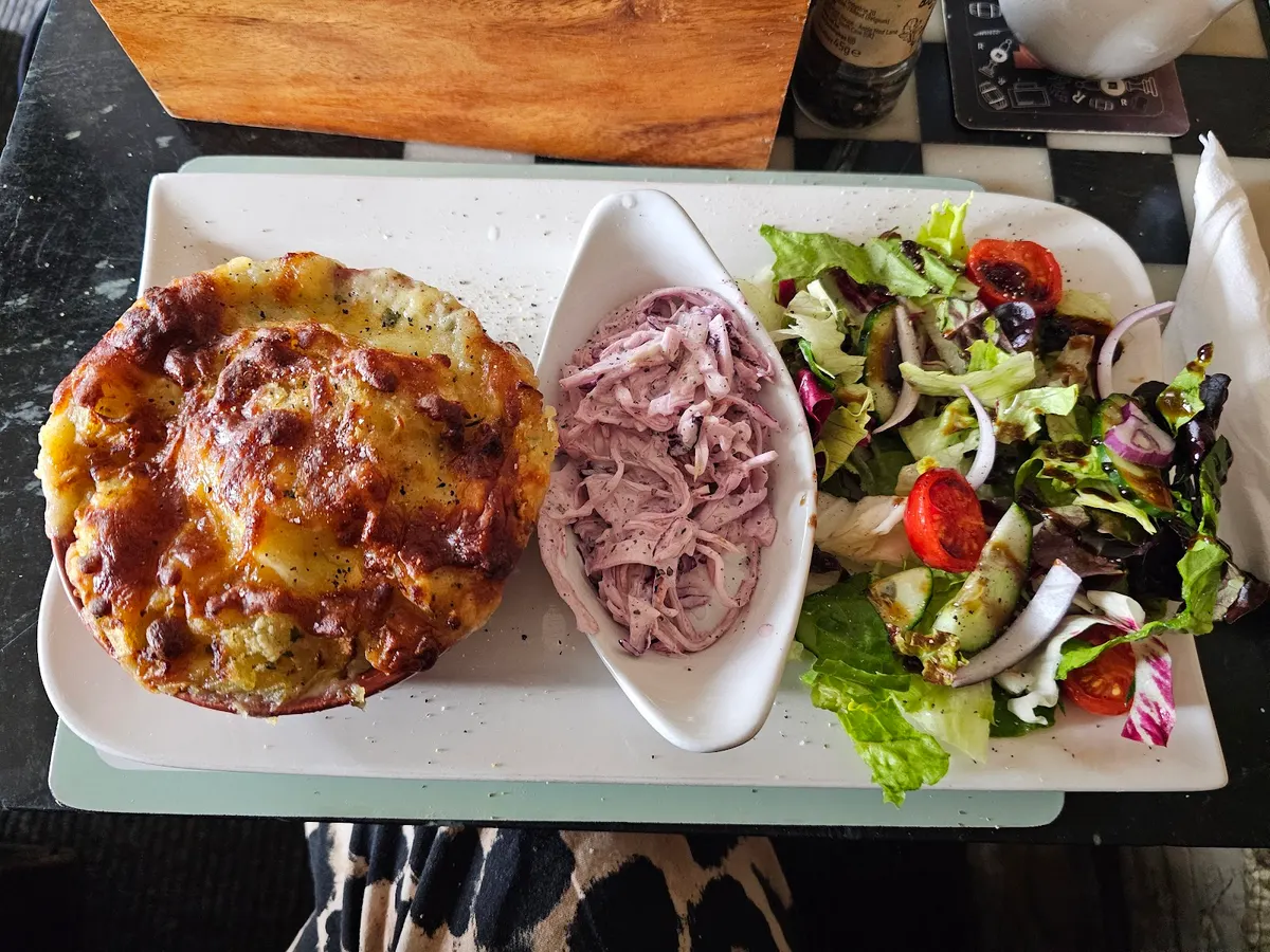 A plated meal with golden-brown pie, shredded pink meat, and fresh salad.