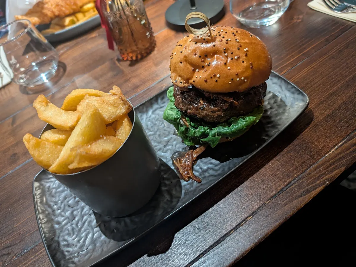 A gourmet burger with seeded bun and crispy chips served on a dark slate plate.