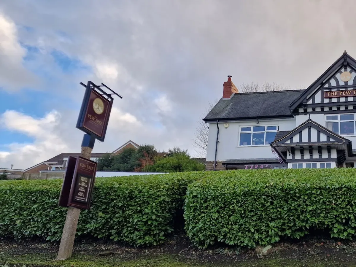 The Yew Tree Inn, a traditional black and white Tudor-style building with a hanging pub sign, behind a green hedge.